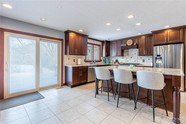 kitchen with sink, appliances with stainless steel finishes, a kitchen breakfast bar, light stone countertops, and a kitchen island