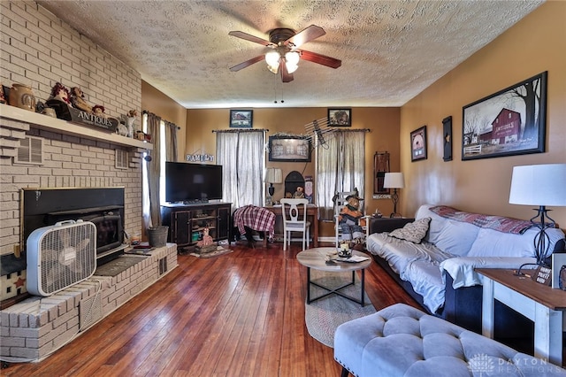 living area with a textured ceiling, ceiling fan, a brick fireplace, and wood-type flooring