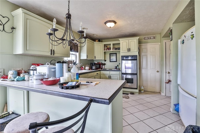 kitchen featuring light tile patterned floors, freestanding refrigerator, a peninsula, cream cabinetry, and stainless steel double oven