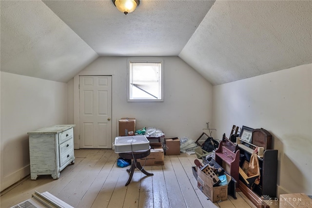 additional living space with light wood-style floors, vaulted ceiling, and a textured ceiling