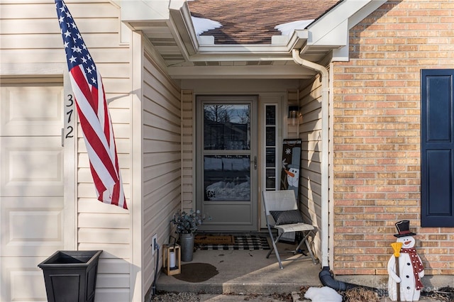 doorway to property featuring a garage, brick siding, and a shingled roof