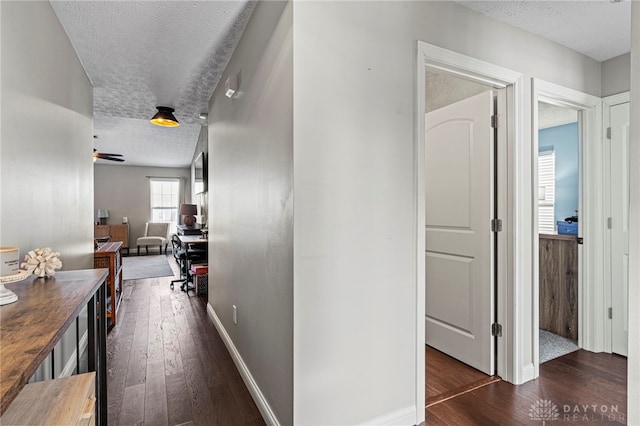 hallway with a textured ceiling, dark wood-style flooring, and baseboards