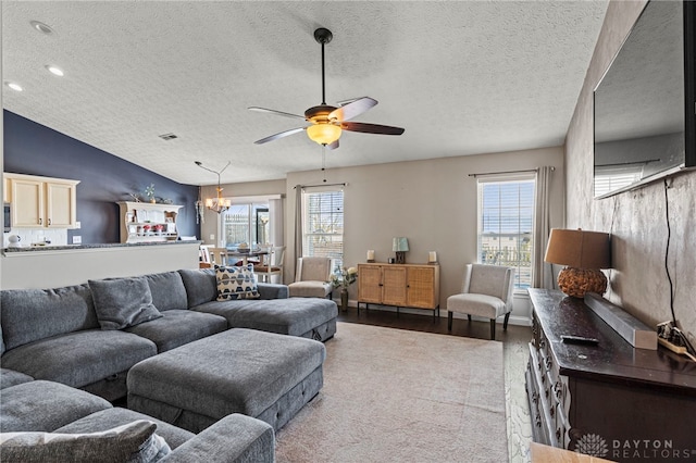 living room featuring light wood finished floors, baseboards, visible vents, lofted ceiling, and ceiling fan with notable chandelier