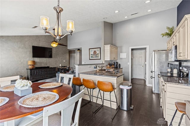 kitchen with cream cabinetry, hanging light fixtures, appliances with stainless steel finishes, open floor plan, and a peninsula