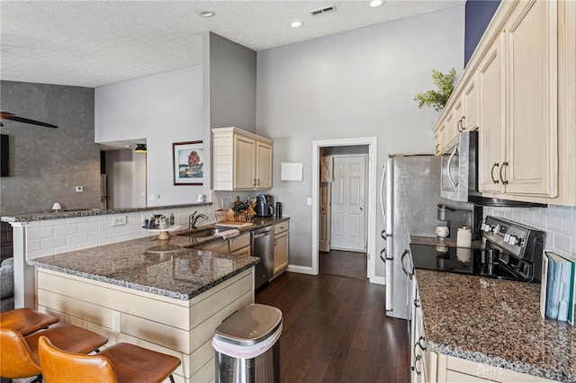 kitchen with a peninsula, a breakfast bar, visible vents, appliances with stainless steel finishes, and dark stone counters