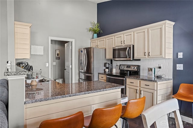 kitchen with a peninsula, appliances with stainless steel finishes, backsplash, dark stone countertops, and a kitchen bar