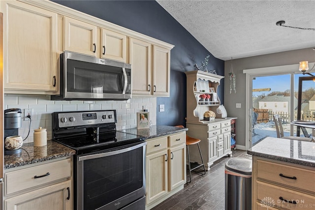 kitchen with dark stone counters, dark wood-type flooring, stainless steel appliances, a textured ceiling, and backsplash