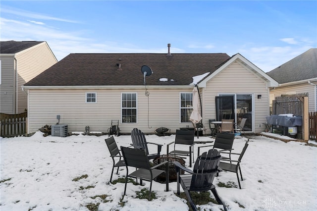 snow covered rear of property featuring a shingled roof, central AC unit, and fence