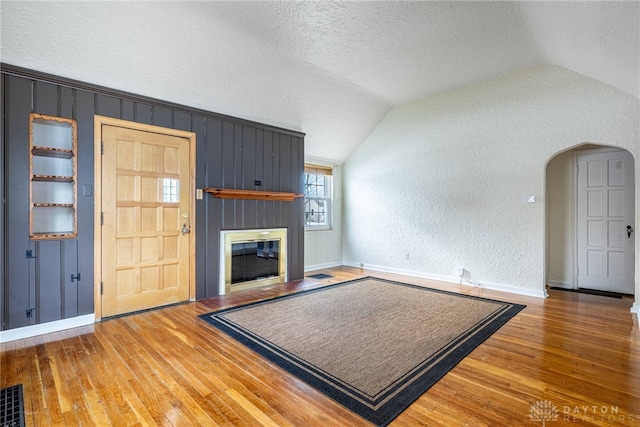 unfurnished living room featuring hardwood / wood-style flooring, vaulted ceiling, and a textured ceiling