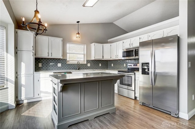 kitchen featuring stainless steel appliances, a center island, white cabinets, decorative light fixtures, and vaulted ceiling