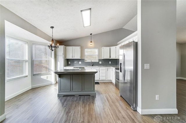 kitchen with backsplash, stainless steel appliances, white cabinets, a kitchen island, and vaulted ceiling