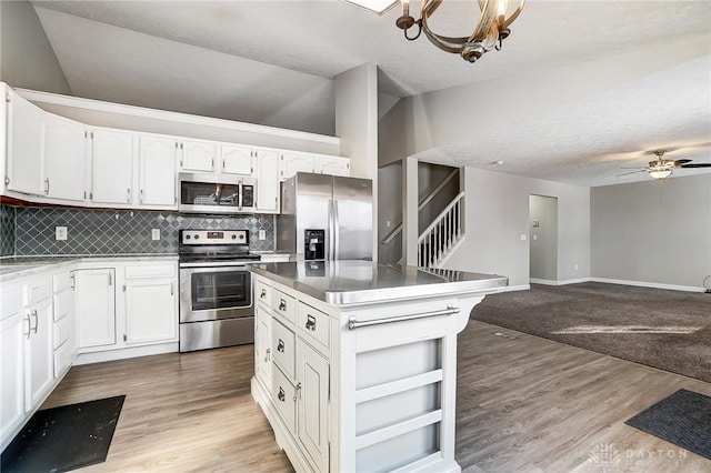 kitchen with stainless steel appliances, vaulted ceiling, backsplash, and white cabinetry