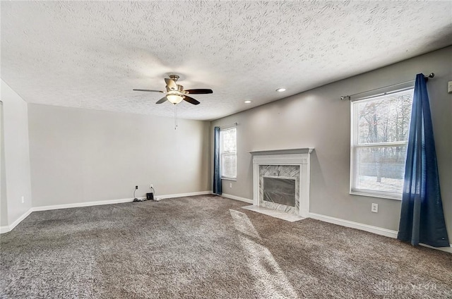 unfurnished living room featuring a premium fireplace, carpet floors, a textured ceiling, and a wealth of natural light