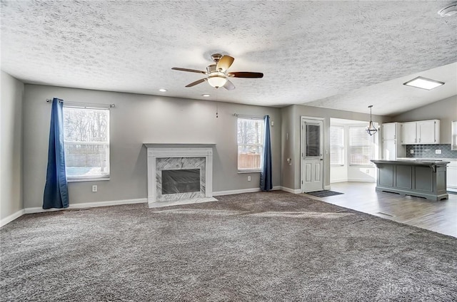 unfurnished living room with vaulted ceiling, carpet flooring, ceiling fan, a high end fireplace, and a textured ceiling