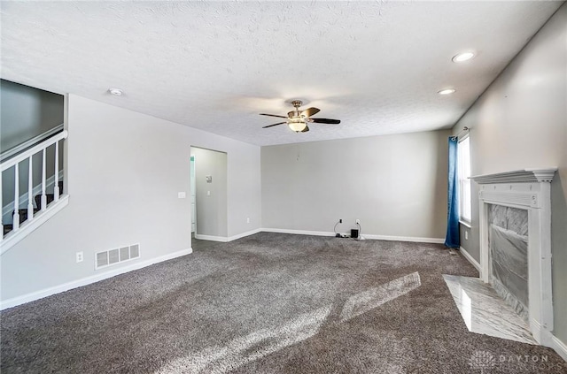 unfurnished living room featuring dark colored carpet, ceiling fan, a fireplace, and a textured ceiling