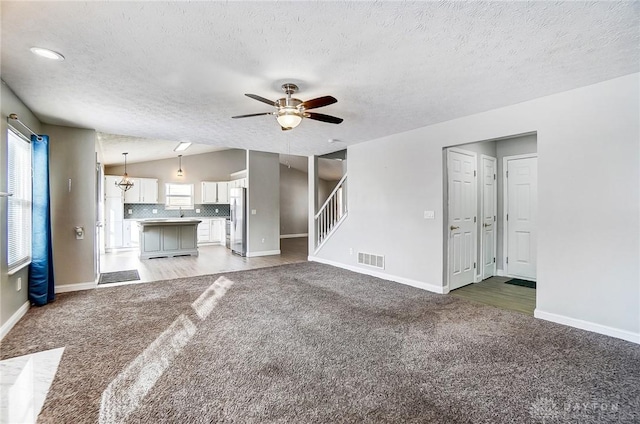 unfurnished living room with lofted ceiling, ceiling fan with notable chandelier, carpet floors, and a textured ceiling