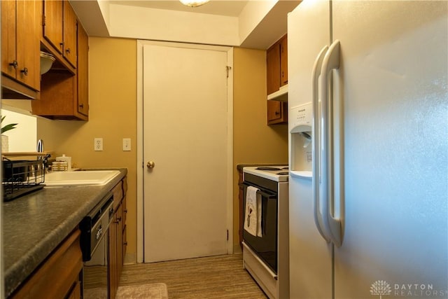 kitchen featuring light wood-style flooring, white appliances, brown cabinets, under cabinet range hood, and a sink