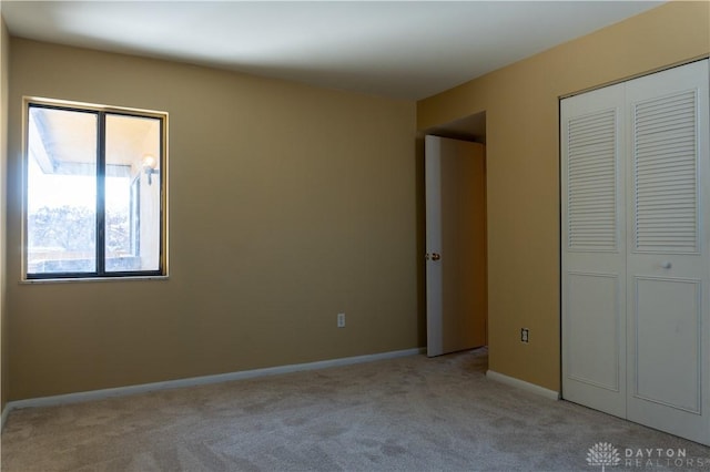unfurnished bedroom featuring light colored carpet, a closet, and baseboards