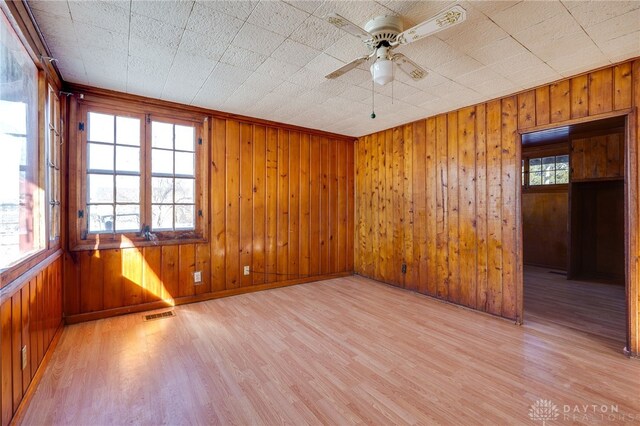 unfurnished room with ceiling fan, wooden walls, and light hardwood / wood-style flooring