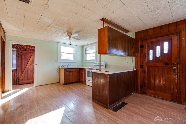 kitchen with sink, wooden walls, white range with electric stovetop, kitchen peninsula, and light wood-type flooring