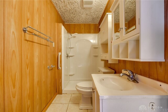 bathroom featuring toilet, a shower, wood walls, vanity, and tile patterned flooring