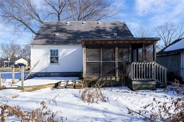 snow covered back of property with a sunroom