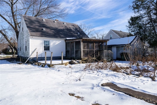 snow covered rear of property featuring a sunroom