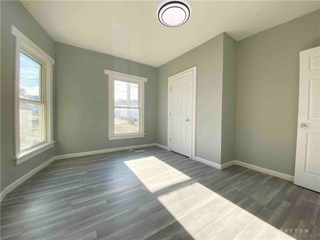 unfurnished bedroom featuring multiple windows, a closet, and dark hardwood / wood-style floors