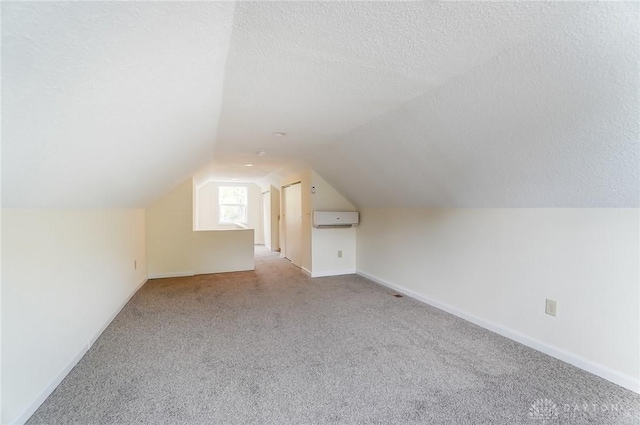 bonus room featuring light carpet, vaulted ceiling, an AC wall unit, and a textured ceiling