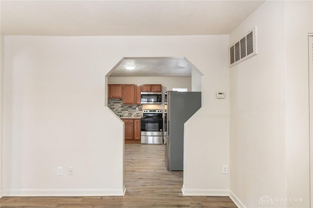 kitchen with tasteful backsplash, appliances with stainless steel finishes, and light hardwood / wood-style floors