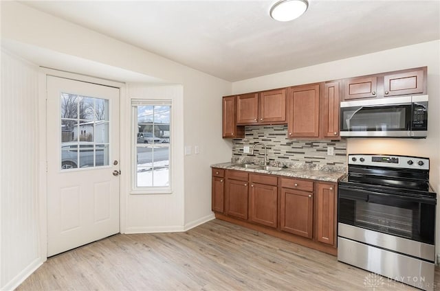 kitchen featuring sink, appliances with stainless steel finishes, tasteful backsplash, light stone counters, and light wood-type flooring