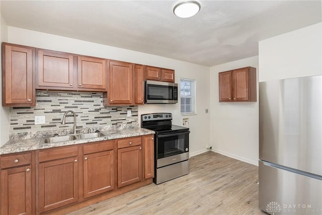 kitchen with light stone counters, sink, light hardwood / wood-style floors, and appliances with stainless steel finishes