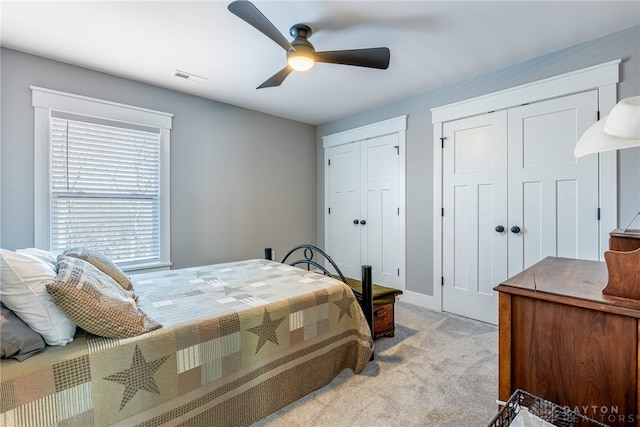 bedroom featuring light carpet, multiple closets, and ceiling fan