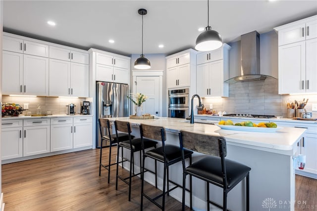 kitchen featuring white cabinetry, pendant lighting, a kitchen island with sink, and wall chimney range hood