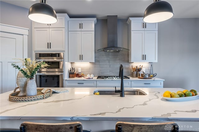 kitchen with decorative light fixtures, double oven, decorative backsplash, and wall chimney range hood