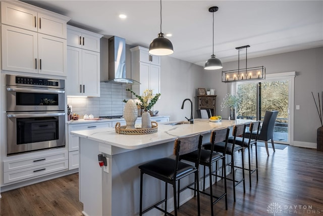 kitchen featuring a center island with sink, white cabinetry, sink, and wall chimney range hood