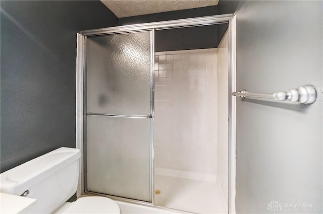 bathroom featuring a textured ceiling, a shower with shower door, and toilet