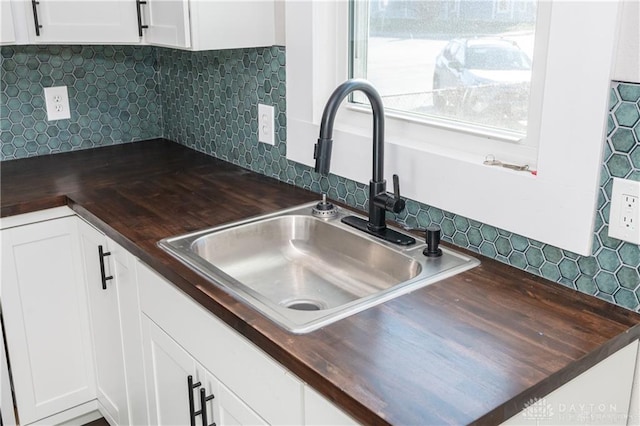 kitchen with tasteful backsplash, wood counters, sink, and white cabinets