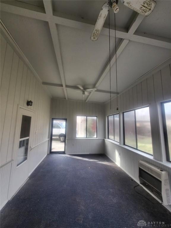 unfurnished sunroom with ceiling fan, heating unit, beam ceiling, coffered ceiling, and a wall mounted air conditioner