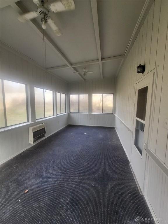 unfurnished sunroom with beamed ceiling, coffered ceiling, a wall unit AC, and ceiling fan