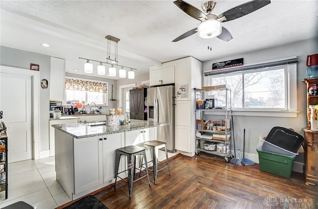 kitchen featuring pendant lighting, a center island, stainless steel refrigerator with ice dispenser, light stone countertops, and white cabinets