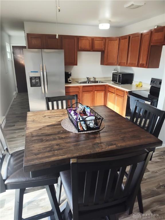 kitchen featuring wood finished floors, a sink, baseboards, light countertops, and black appliances