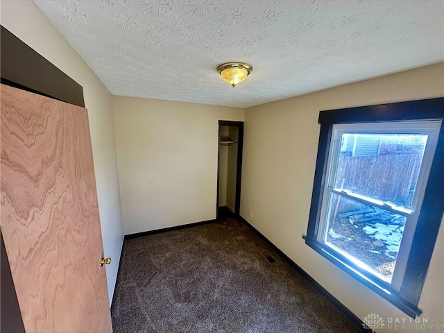 unfurnished bedroom featuring a closet, a textured ceiling, and dark colored carpet