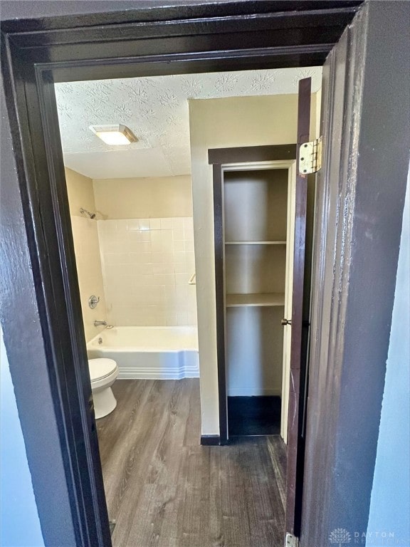 bathroom featuring hardwood / wood-style flooring, bathing tub / shower combination, a textured ceiling, and toilet