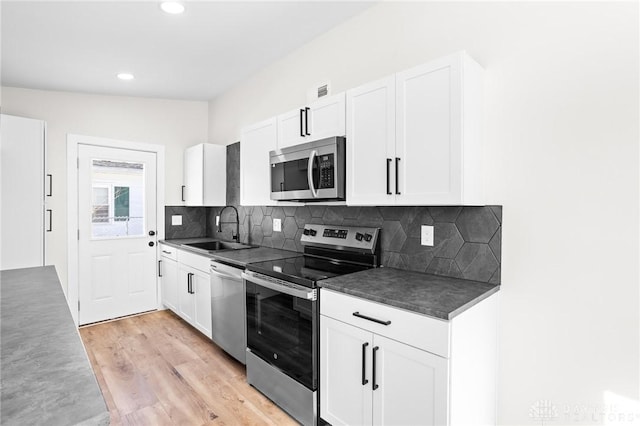 kitchen with sink, light hardwood / wood-style flooring, appliances with stainless steel finishes, backsplash, and white cabinets