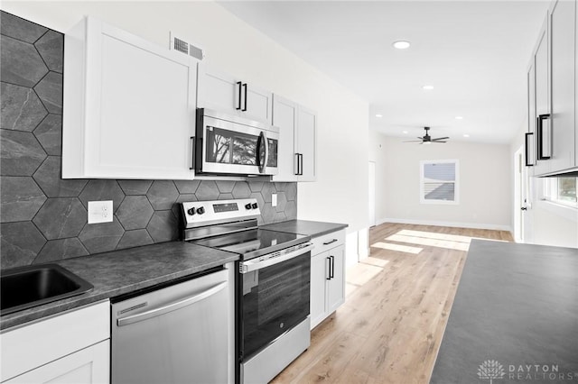 kitchen featuring ceiling fan, appliances with stainless steel finishes, white cabinets, decorative backsplash, and light wood-type flooring