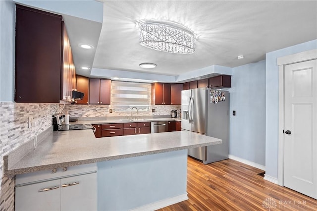 kitchen featuring sink, stainless steel appliances, tasteful backsplash, kitchen peninsula, and light wood-type flooring