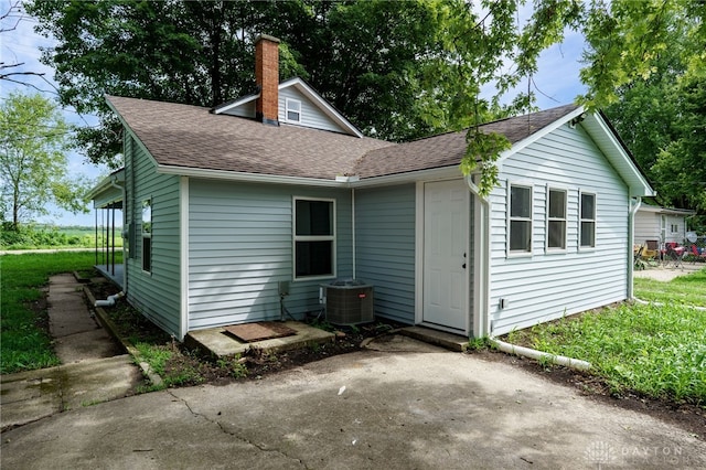 exterior space featuring cooling unit, a chimney, and a shingled roof