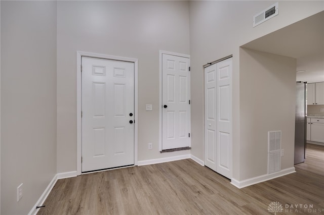 foyer with a high ceiling, baseboards, visible vents, and light wood finished floors