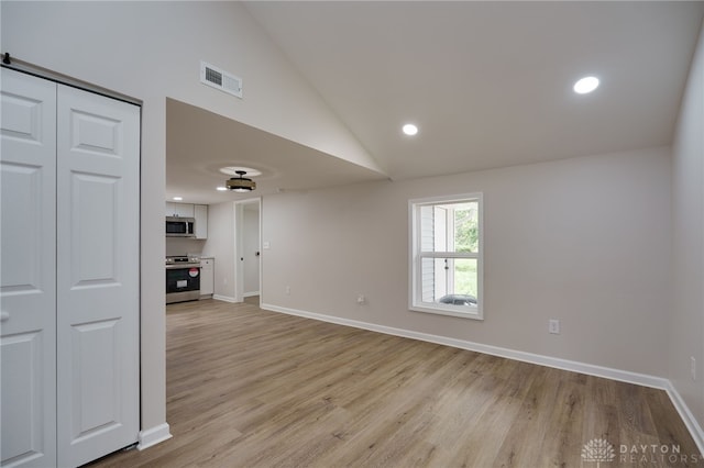 empty room with visible vents, baseboards, light wood-style floors, and vaulted ceiling